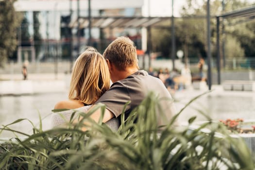 An adult mature happy romantic couple in love sitting on bench outdoors in city street park. A blonde caucasian man and woman spend time together. Senior wife and husband walking outside