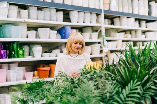 Gardening, planting and shopping concept. Beautiful mature adult woman choosing houseplants and pots in greenhouse or garden centre. Senior buying flowers plants at market store in mall.