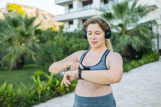 Fat woman checking time or heart rate from smart watch. Exercise or running outdoors for weight loss idea concept. Wellness and wellbeing concept