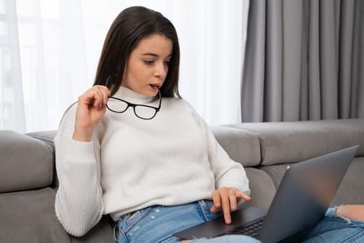 Happy millennial girl working on the laptop at home. Young woman playing game, ordering products, shopping online via internet.