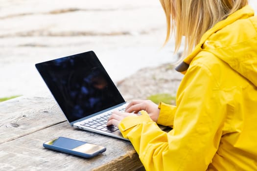 Remote worker relaxing near the lake and using a laptop. Working or studying over a laptop and smartphone.