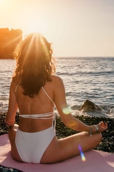 Young woman in swimsuit with long hair practicing stretching outdoors on yoga mat by the sea on a sunny day. Women's yoga fitness pilates routine. Healthy lifestyle, harmony and meditation concept.