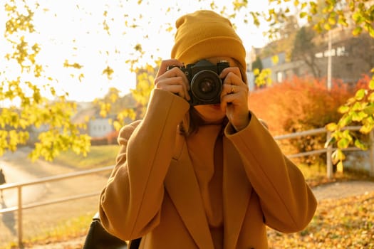 A woman photographer takes a photo on a retro camera in an autumn forest, front view. Autumn photography concept