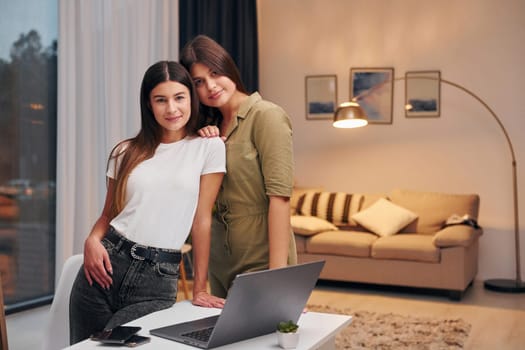 Two women in casual clothes is standing indoors at home.