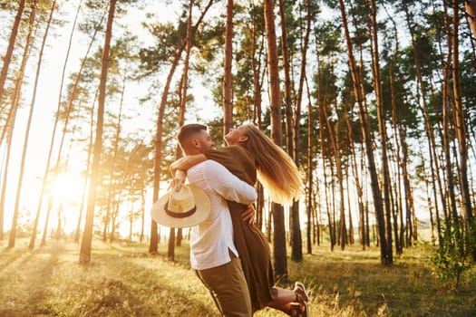 Against background with sunshine. Happy couple is outdoors in the forest at daytime.