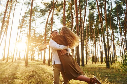 Against background with sunshine. Happy couple is outdoors in the forest at daytime.