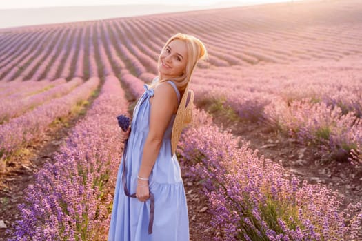 Woman lavender field sunset. Romantic woman walks through the lavender fields. illuminated by sunset sunlight. She is wearing a blue dress with a hat