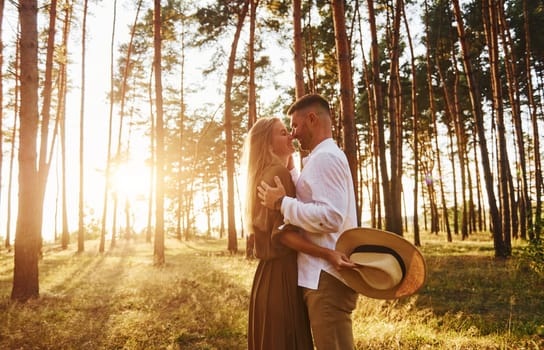 Man is in white shirt and woman in dress. Happy couple is outdoors in the forest at daytime.