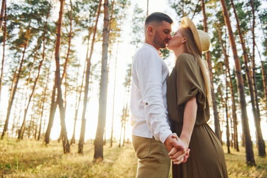 Holding each other by the hands. Happy couple is outdoors in the forest at daytime.