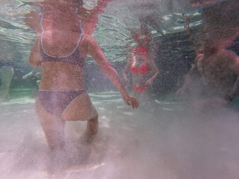 Irrecognizable people having fun in the crystal-clear water filled with bubbles of a Fervedouro, a unique experience where the sandy bottom creates a quicksand effect. Underwater photography.