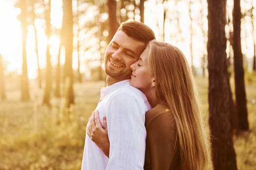 Illuminated by sunlight. Happy couple is outdoors in the forest at daytime.