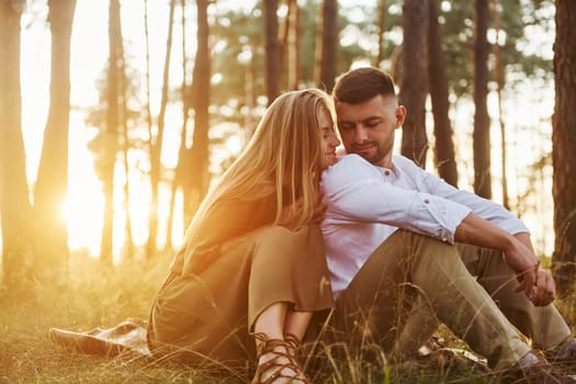 Sitting on the ground. Happy couple is outdoors in the forest at daytime.