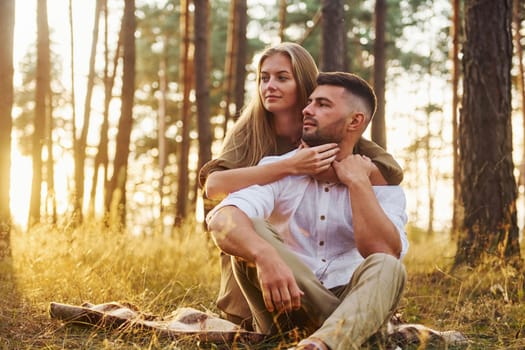 Sitting on the ground. Happy couple is outdoors in the forest at daytime.