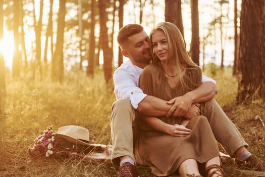 Sitting and embracing each other. Happy couple is outdoors in the forest at daytime.