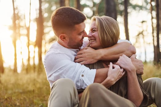 Sitting and embracing each other. Happy couple is outdoors in the forest at daytime.