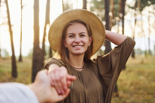 Woman holding man's hand. Happy couple is outdoors in the forest at daytime.