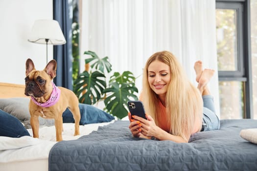 Holding phone. Woman with pug dog is at home at daytime.