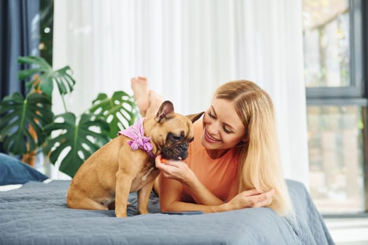 Laying down on bed. Woman with pug dog is at home at daytime.