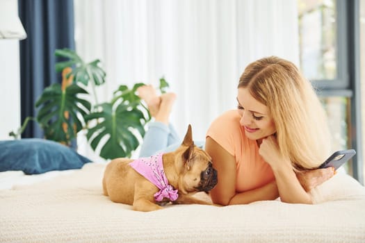 Laying down on bed. Woman with pug dog is at home at daytime.