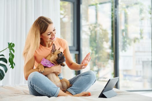 With tablet on bed. Woman with pug dog is at home at daytime.