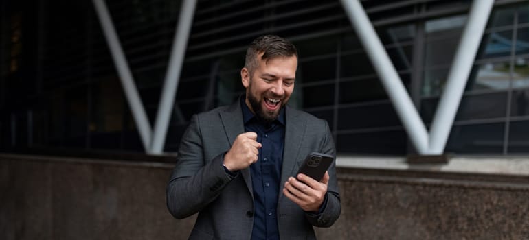 happy freelancer man with a smartphone in his hands smiling against the backdrop of the building.