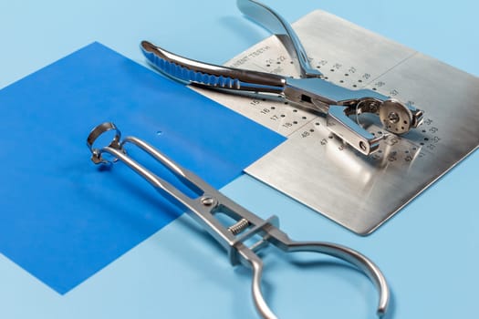 Dental hole punch, the metal plate, the rubber dam and the rubber dam forceps on the blue background. Medical tools concept.