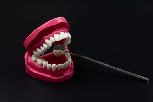 Layout of the human jaw with a metal mouth mirror on the black background. Dental instruments for dental treatment.