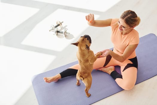 On fitness mat. Woman with pug dog is at home at daytime.