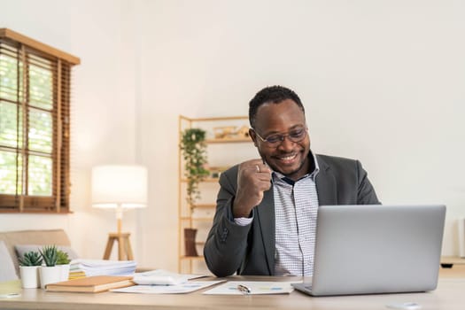 Success at work, good deal. African-American guy looks at the laptop screen, screams excitedly and raises his fists in a victory gesture at home...