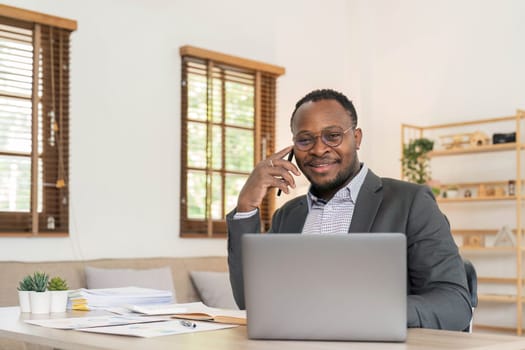 Portrait of handsome African black young business man working on laptop and talking phone at office desk...