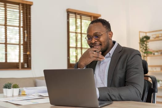 Portrait of handsome African black young business man working on laptop at office desk...