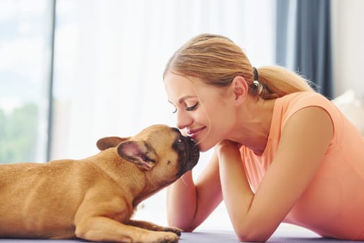 Laying down on the mat. Woman with pug dog is at home at daytime.