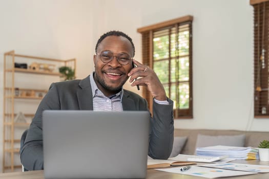 Portrait of handsome African black young business man working on laptop and talking phone at office desk...