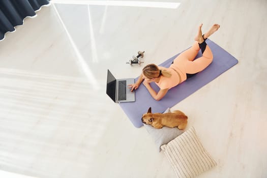 Top view of woman with pug dog and laptop that is at home at daytime.