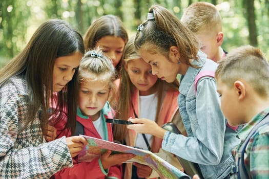 With map. Kids in green forest at summer daytime together.