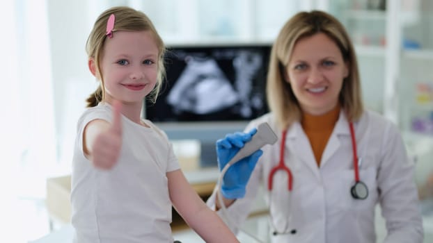 Little girl showing thumbs up at doctor appointment with ultrasound diagnostics in clinic. High quality professional instrumental medical examination in children concept