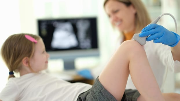 Doctor pediatrician conducting ultrasound examination of knee joint of child in clinic closeup. Diagnosis of rheumatic diseases in children concept