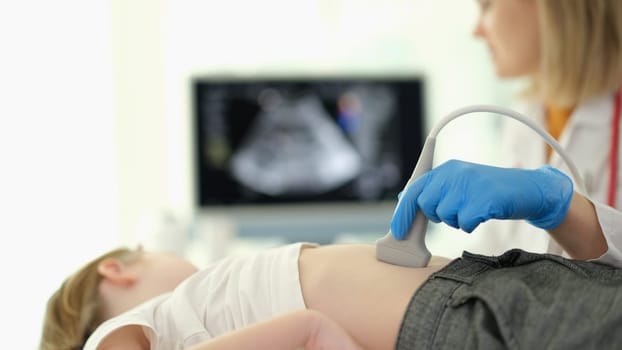 Doctor gastroenterologist making ultrasound examination of liver and pancreas to child in clinic closeup. Diagnosis and treatment of diseases of internal organs in children concept