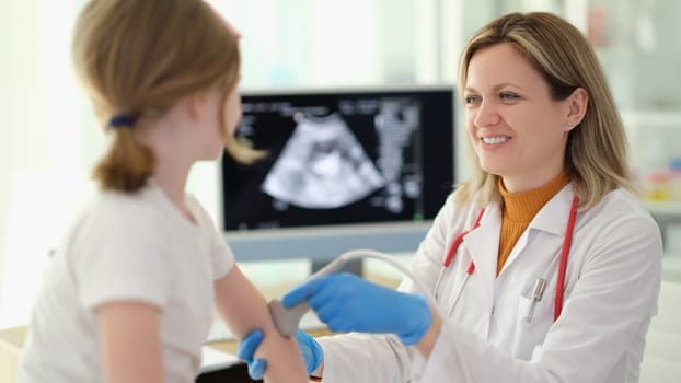 Doctor traumatologist making ultrasound examination of elbows of little girl in clinic. Diagnosis and treatment of rheumatoid arthritis in children concept