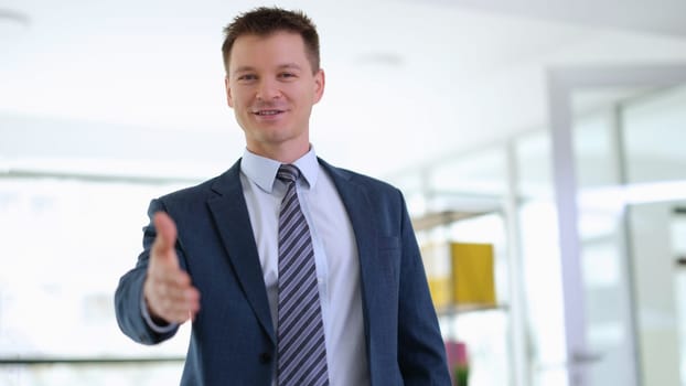 Successful businessman in suit and tie holding out hand for handshake in office. Work with partners concept