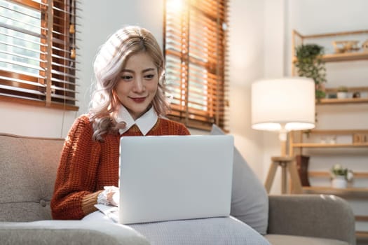 woman smiling and using laptop computer at home sitting comfortably on a sofa in living room. Smart working female people notebook. Surfing the web. Enjoying technology and connection.