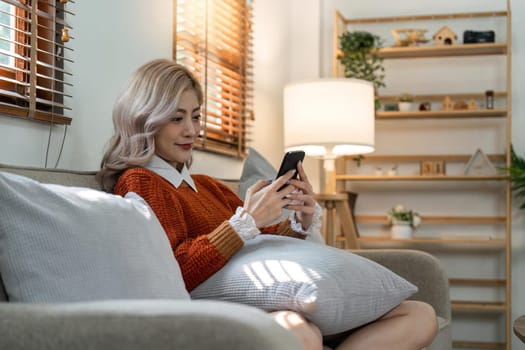 Happy young asian woman on mobile phone while sitting a couch in living room at home, Shopping online via website.