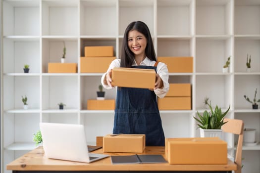 Young business woman working online e-commerce shopping at her shop. Young woman seller prepare parcel box of product for deliver to customer. Online selling.