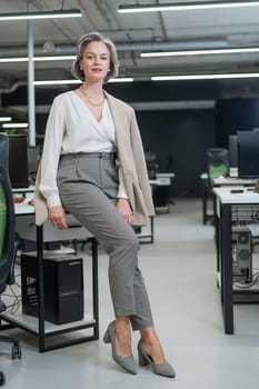 Portrait of a beautiful gray-haired caucasian woman leaning against the desktop in the office