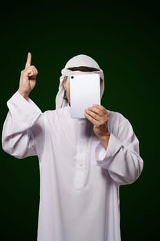Muslim anonymous concept. Arab person holds digital tablet, face covered, index finger up, representing the concept of Islamic censorship online. Image portrays issues of privacy, security, and anonymity in the digital world. High quality photo