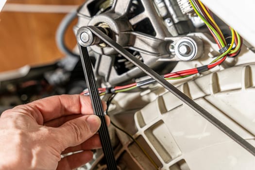 The repairman checks the condition of the drive belt of the electric motor of the electric washing machine. close-up. repair of a used washing machine. Belt drive pulley. vibrations and rotations. Drum drive