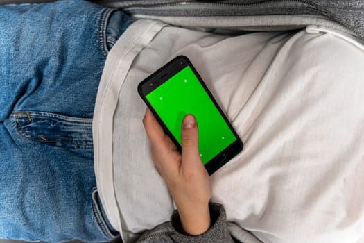 top view of a girl lying on the couch and using a smartphone. the girl is holding a smartphone with a green screen. smartphone with chromakey.web browsing on the internet. Dependence on gadgets. Chat communication. the choice of purchases in the online market