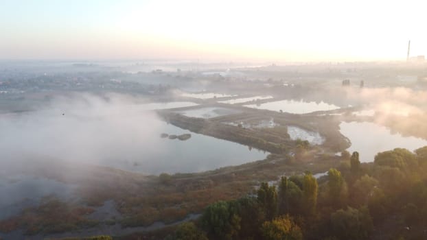 Lakes, artificially created water ponds for growing fish farming with morning mist on an early summer sunny morning. Nature scenery, natural landscape. Sunlight, sunshine. Top view. Aerial drone view.