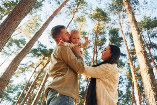 View from below. Happy family of father, mother and little daughter is in the forest.