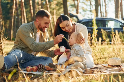 Eating some food. Happy family of father, mother and little daughter is in the forest.